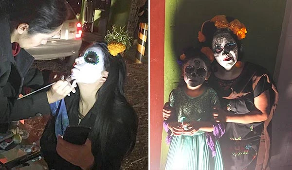 Duas crianças e uma adulta se fantasiando o Dia dos Mortos em Puebla, com maquiagem de caveira mexicana, vestindo roupas coloridas e acessórios de fantasia, comemorando a data.