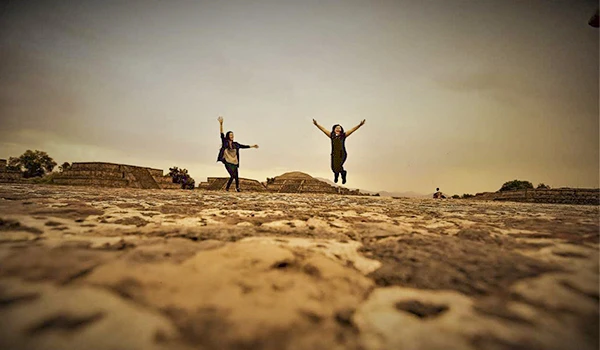 Duas pessoas comemorando com braços abertos em um cenário ao ar livre, capturadas em um momento de felicidade e liberdade, sob um céu de tom quente.
