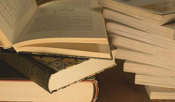 Foto de vários livros empilhados uns sobre os outros em bibilioteca.