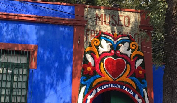 Fachada de um museu com pintura colorida de coração, flores e elementos tradicionais, na cidade de Frida, com uma placa de boas-vindas.