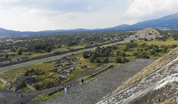 Vista do sítio arqueológico na região de Chichen Itza, com as pirâmides e áreas de construção antigas rodeadas por vegetação e paisagens montanhosas ao fundo. Pirâmides do Sol e da Lua.