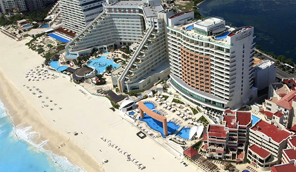 Imagem aérea de um resort de luxo à beira-mar na praia, com piscinas, acomodações modernas e vista para o oceano, ideal para a Lua de Mel em Cancun.