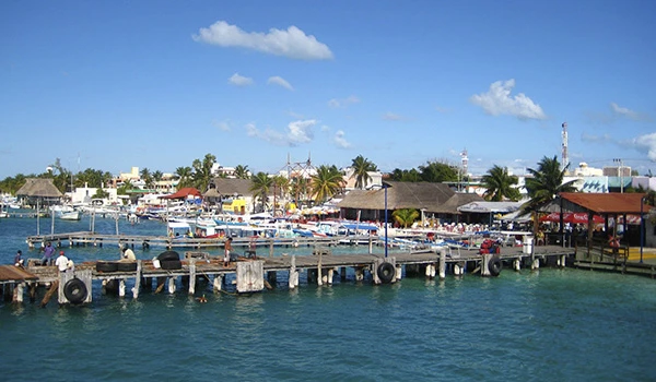 Linda vista de um píer de pesca e marina em uma cidade litorânea com barcos, lojas e palmeiras sob céu azul com nuvens, na Lua de Mel em Cancun.