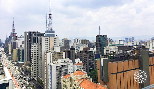 Vista panorâmica da arquitetura moderna e urbana de São Paulo, destacando edifícios altos e torres de comunicação, sob um céu nublado.
