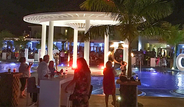 Pessoas curtindo uma festa ao ar livre perto da piscina, com iluminação urbana e uma estrutura moderna ao fundo.