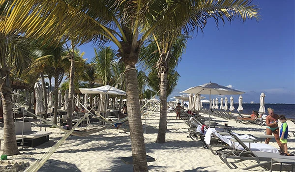 Praia de areia branca com espreguiçadeiras e guarda-sóis sob palmeiras, cenário ensolarado perfeito para relaxar na Lua de Mel em Cancun.