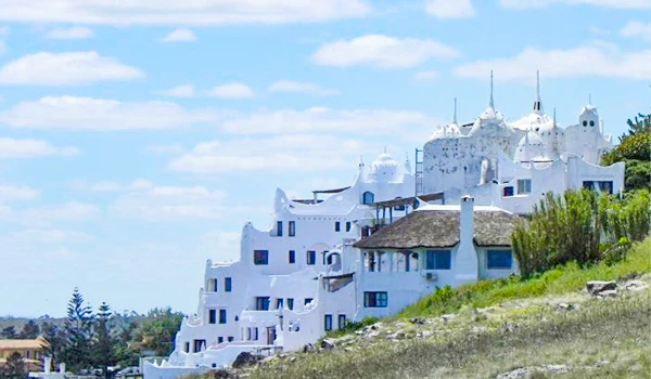 Imagem de uma casa branca em estilo arquitetônico único em uma encosta, com céu azul ao fundo e vegetação ao redor, ideal para decoração de interiores e design de casas. Cassino Punta del Este.