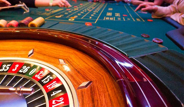 Imagem de uma mesa de cassino com uma roleta de roleta americana e fichas de apostas, com pessoas jogando. Cassino Punta del Este.