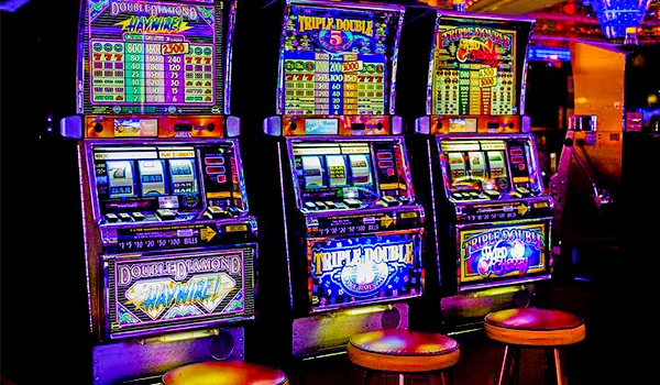 Máquinas caça-níqueis de casino com luzes coloridas em uma sala de jogos, promovendo jogos de azar como Double Diamond, Triple Double e Double Double. Cassino Punta del Este.