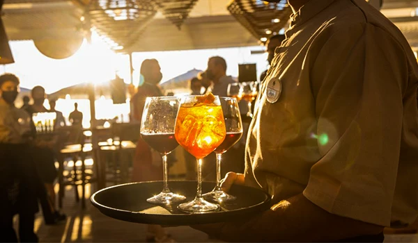 Garçom servindo drinks com gelo em um bar ao pôr do sol, ambiente animado e descontraído, perfeito para momentos de lazer e socialização.