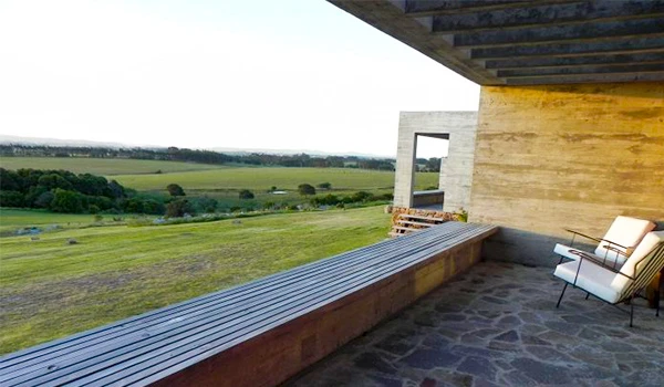 Vista panorâmica de uma varanda moderna com móveis de descanso, vista para um campo aberto verde e céu claro, ideal para relaxar ao ar livre.