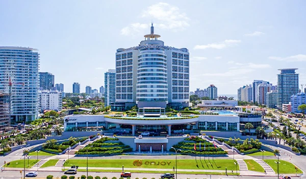 Hotel moderno com fachada de vidro, cercada por áreas verdes bem cuidadas e uma cidade movimentada ao fundo. Cassino Punta del Este.