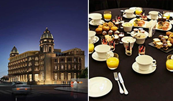 Imagem de um hotel ao entardecer ao lado de uma mesa de café da manhã com café, sucos e alimentos variados.