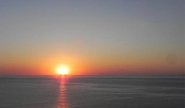 Por do sol no horizonte sobre o oceano, com céu colorido em tons de laranja, rosa e azul, refletindo na água calma, criando uma cena pacífica e relaxante. Cassino Punta del Este.