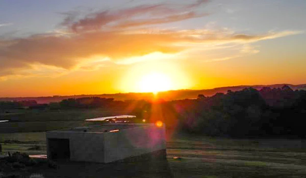 Imagem de um pôr do sol sobre um campo aberto, com céu colorido em tons de laranja e amarelo, criando uma atmosfera serena e inspiradora.
