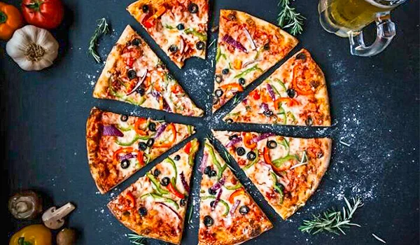 Pizza redonda cortada em oito fatias, coberta com queijo, tomate, azeitonas, pimentões e cebola, sobre uma superfície escura.