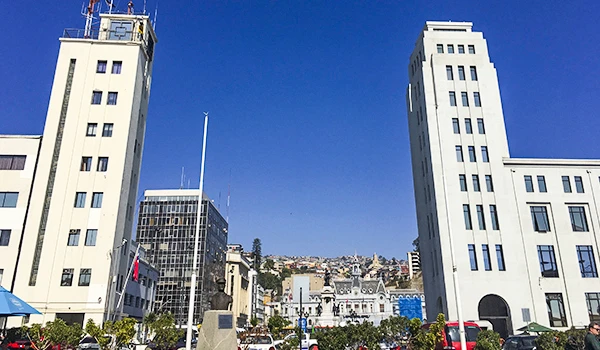 Imagem de arranha-céus no centro de uma cidade com céu azul claro ao fundo, destacando edifícios altos e modernos em um cenário urbano.