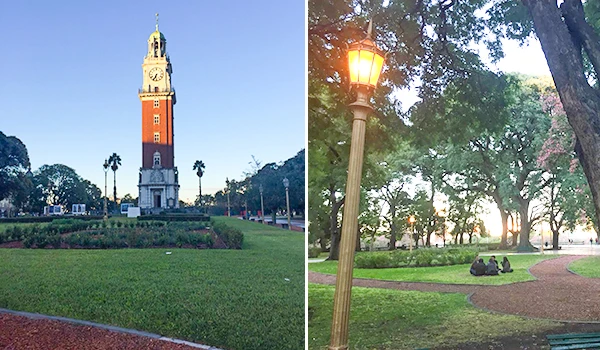 Imagem de um parque ao entardecer com um relógio antigo em torre, árvores, grama bem cuidada e uma luminária de rua acesa, cenário tranquilo e acolhedor.