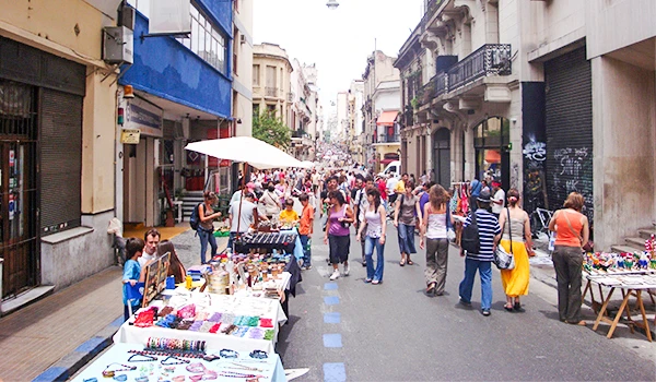 Rua de feira em uma cidade movimentada com várias barracas de artesanato e pessoas caminhando. Viagem para Buenos Aires.