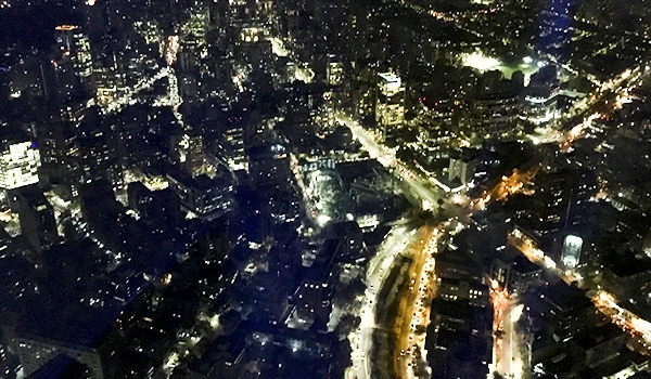 Vista noturna de uma cidade iluminada com prédios altos, ruas movimentadas e luzes brilhantes, mostrando a beleza urbana à noite.