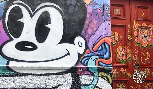 Grafite colorido com personagem de desenho animado em uma parede, ao lado de uma porta decorada com flores e detalhes artísticos.