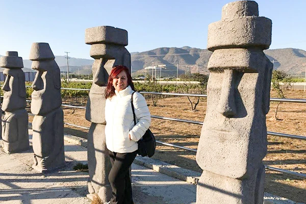 Deusa Rodrigues próximo às estátuas moais, pontos turísticos famosos no Chile, com montanhas ao fundo e céu azul claro.