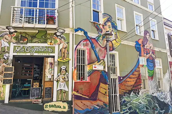 Arte de rua vibrante com mural de um personagem de fantasia colorido na fachada de um restaurante chamado La Goffeteria, em uma rua movimentada. Grafites de Valparaíso.
