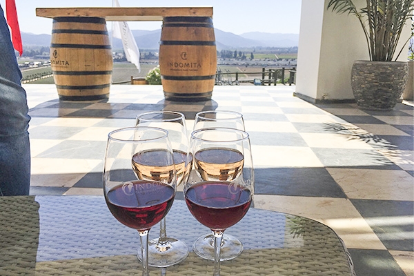 Taças de vinho rosé em uma varanda com vista para o campo e barris de vinho ao fundo. Vinícolas no Chile, qual visitar?