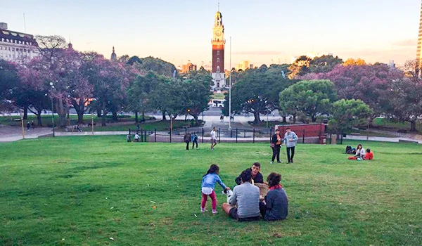 Pessoas desfrutando de um parque em Buenos Aires, árvores verdes e um céu ao entardecer, cenário calmo e convidativo para lazer ao ar livre.