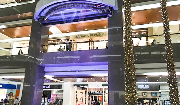 Imagem do interior de um shopping com iluminação decorativa, lojas renomadas e árvores iluminadas, transmitindo uma atmosfera festiva e moderna.