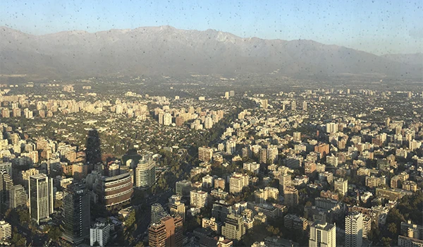 Imagem de uma vasta paisagem urbana com muitos edifícios do alto do Sky Costanera, com montanhas ao fundo, sob céu claro.