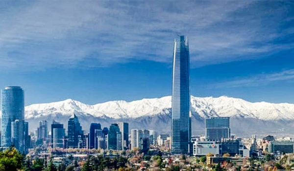 Vista panorâmica do skyline de Santiago, com o edifício Costanera Center ao centro e as Cordilheiras dos Andes ao fundo em um dia ensolarado.