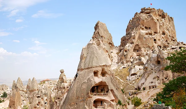 Formações rochosas com construções escavadas na pedra em Capadócia, na Turquia, sob um céu azul com nuvens esparsas.