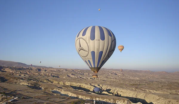 Balões de ar quente sobrevoam a paisagem rochosa da Capadócia, na Turquia, sob um céu azul e limpo.