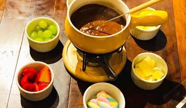 Tábua de chocolate quente com diversas frutas e doces ao redor, ideal para um café da tarde aconchegante, destacando a preparação de bebidas quentes e acompanhamentos.