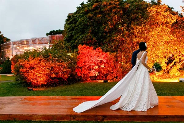 Casal de noivos em cerimônia ao ar livre, com decoração de árvores coloridas e iluminação quente. Lua de Mel em Campos do Jordão.