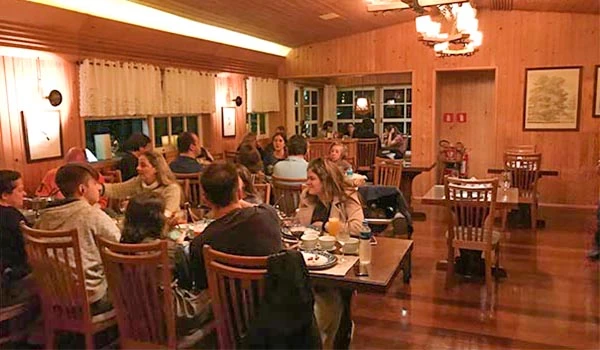 Grupo de pessoas jantando em restaurante aconchegante com decoração de madeira, mesas bem arrumadas e ambiente animado, perfeito para encontros sociais.