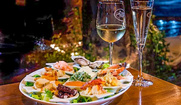 Prato de frutos do mar e taças de vinho branco em jantar romântico, com iluminação acolhedora e fundo natural ao ar livre. Lua de Mel no Chile.