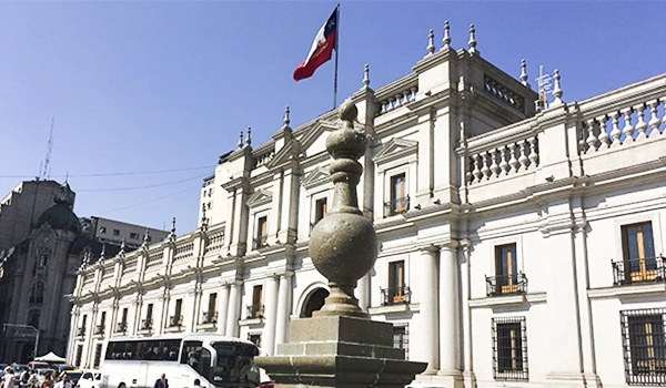 Fachada do Palácio de La Moneda em Santiago do Chile, com a bandeira chilena ao topo e céu claro ao fundo. Lua de Mel no Chile.
