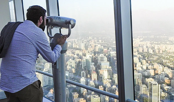 Homem observando a cidade por um telescópio em um edifício alto com vista panorâmica de prédios e arranha-céus na cidade.