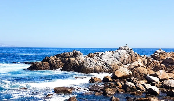 Imagem de uma paisagem costeira com rochas ao lado do mar azul sob céu claro, ideal para quem busca tranquilidade e contato com a natureza.
