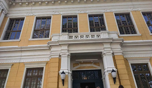 Fachada de um edifício clássico com colunas ornamentais amarelas e janelas de vidro, destacando detalhes arquitetônicos históricos, ideal para imóvel antigo ou comercial. Viagem à Botucatu e Barra Bonita.