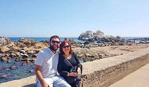 Deusa Rodrigues e Rafael passeando na praia com vista para o mar e rochas ao fundo, aproveitando um dia ensolarado. Viña del Mar o que fazer.