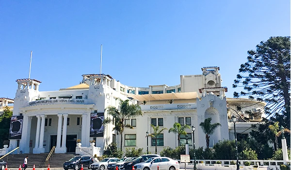 Fachada de uma prédio em Viña del Mar, com arquitetura histórica e área de estacionamento na frente, cercada por árvores e céu claro.