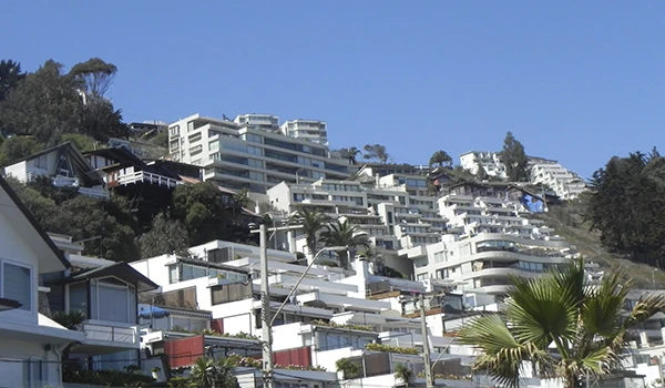Imagem de uma encosta urbanizada com modernas residências brancas e árvores, cenário de construção de casas e edifícios em uma área de relevo acentuado.