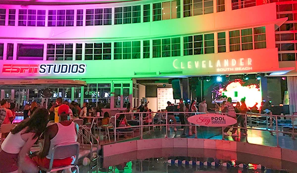 Cleveland South Beach com pessoas curtindo à beira da piscina, iluminação colorida no edifício e música ao vivo em uma noite animada.