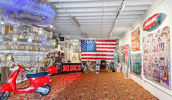 Galeria de arte com decoração vibrante, destaque para bandeira dos Estados Unidos na parede, iluminação elegante com lustre de cristal, e objetos diversos de arte moderna.