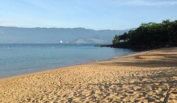 Imagem de uma praia tranquila com areia dourada, águas calmas e vista para montanhas ao fundo. Perfeito para descanso e lazer.