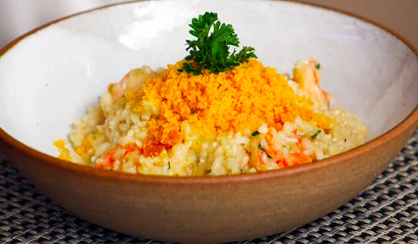 Prato de arroz à grega bem decorado com salsinha e queijo ralado, servido em uma tigela de cerâmica em uma mesa de palha. Perfeito para uma refeição deliciosa.
