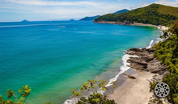 Praia tranquila com águas cristalinas e areia dourada, rodeada por vegetação verdejante e colinas ao fundo, em um cenário paradisíaco.
